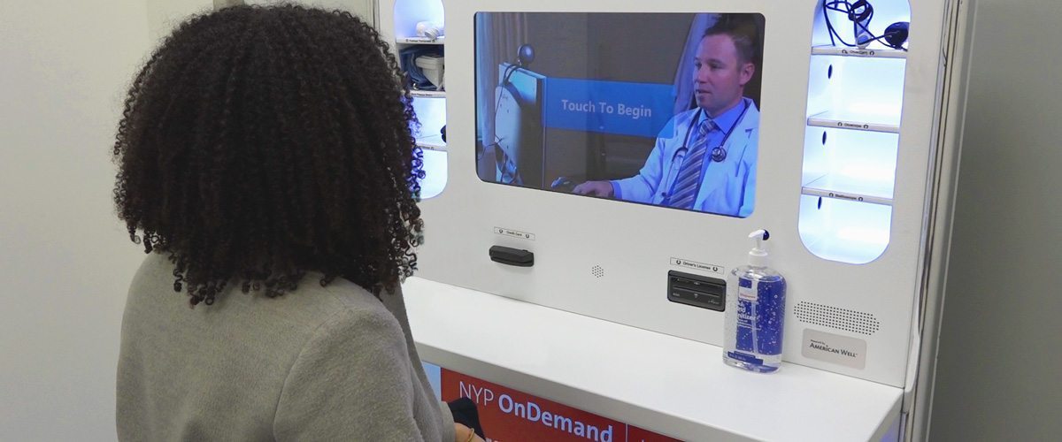 A woman using a telemedicine kiosk to speak with a healthcare provider