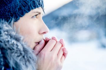 A chilly woman breathing warm air into her hands