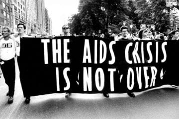 Marchers with a banner that says "The AIDS Crisis Is Not Over"