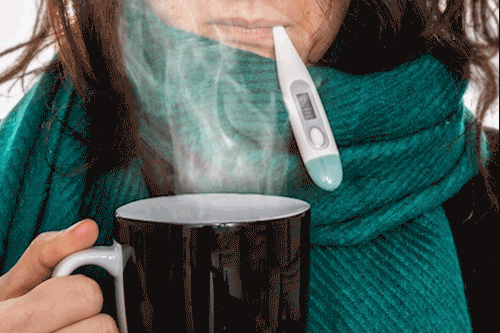 Woman checking temperature while holding steaming cup of tea