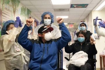 Patients in wheelchairs wearing face masks with their hands up in celebration