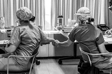 Two healthcare workers holding hands while receiving the COVID-19 vaccine