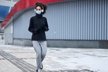 Woman running outdoors, wearing a mask.