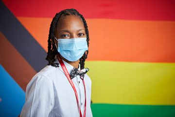 Healthcare worker standing in front of Pride Progress flag to celebrate Pride Month.