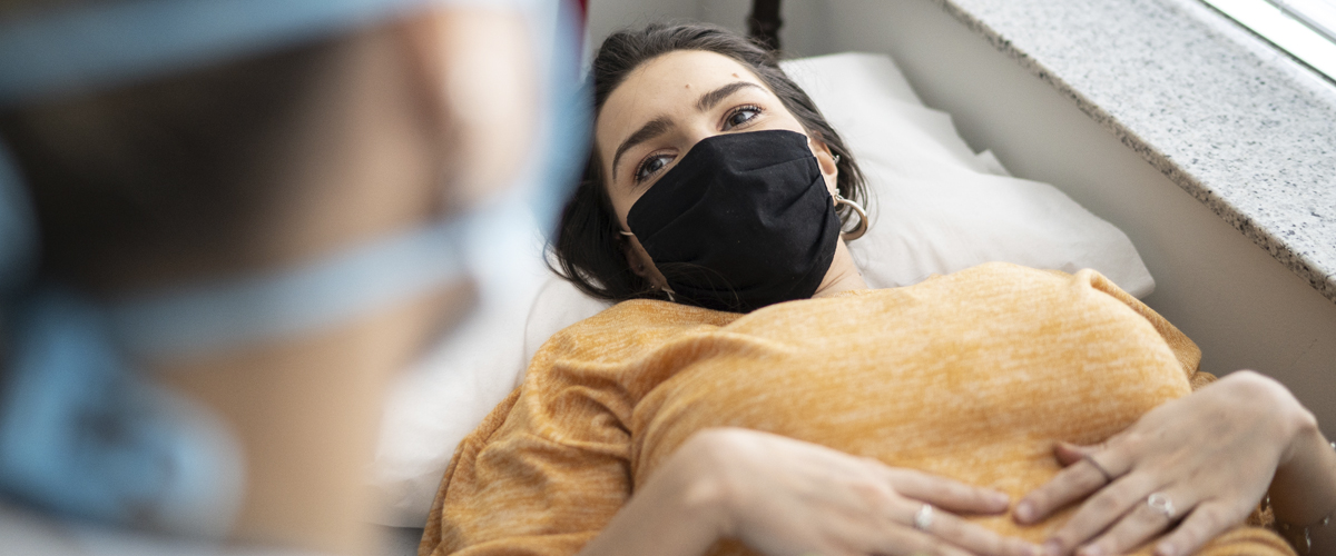A teenager with a black face mask at their first gynecology appointment looks at doctor