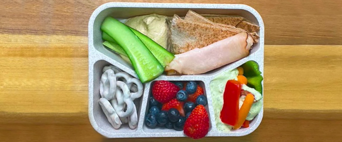 bento lunch box idea with vegetables, fruit, turkey roll-ups, hummus