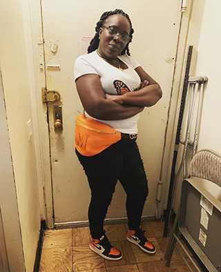 Rachel Harper posing in front of a door with an orange fanny pack carrying her LVAD battery.