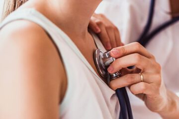 Doctor with stethoscope on woman's chest for women's heart health