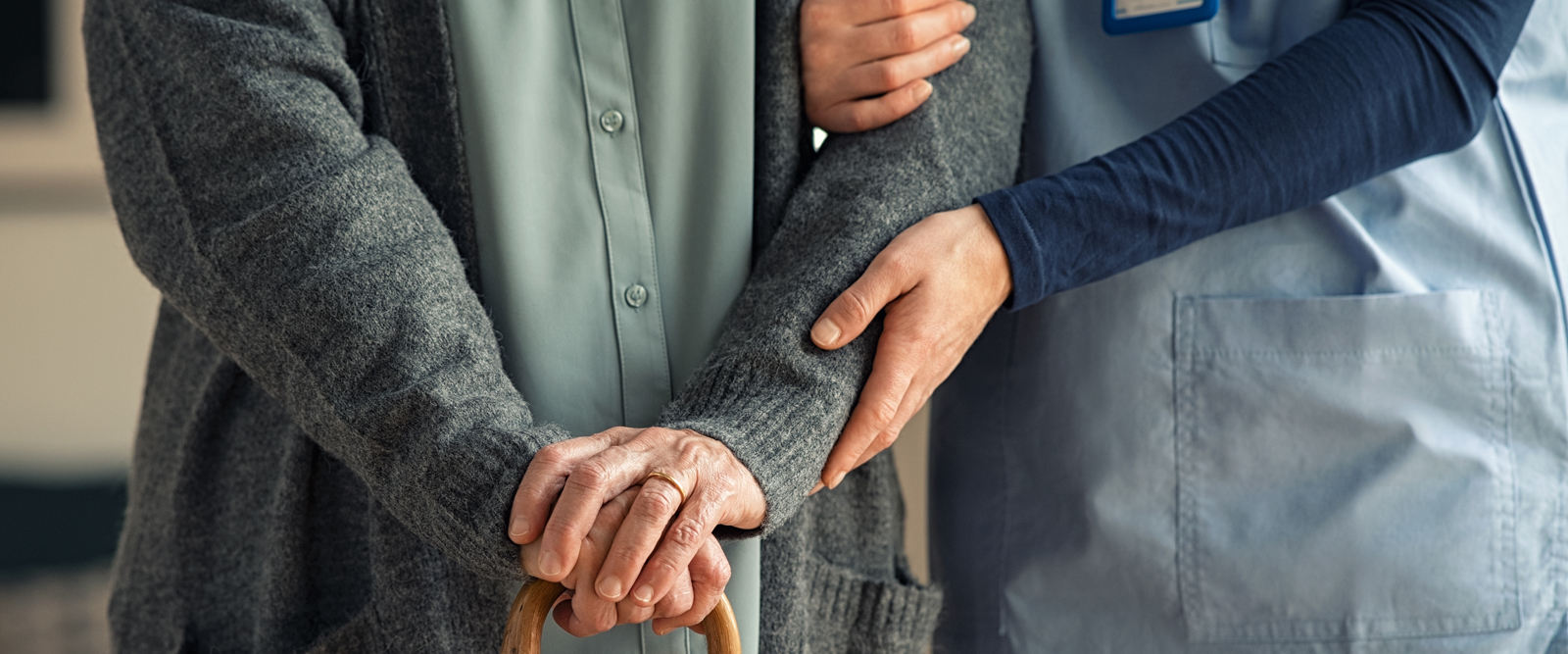 A caregiver holding onto a person with a cane.