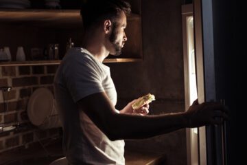 Person standing in front of a refrigerator looking for something to eat late at night.