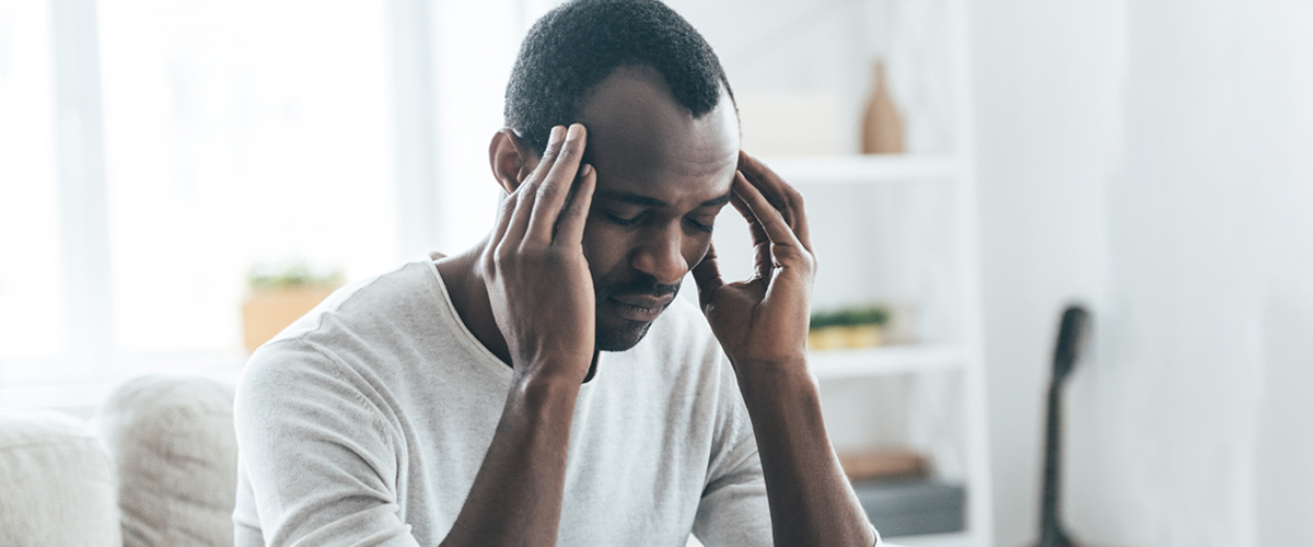 African American man with migraine headache holds his head.