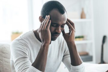 African American man with migraine headache holds his head.