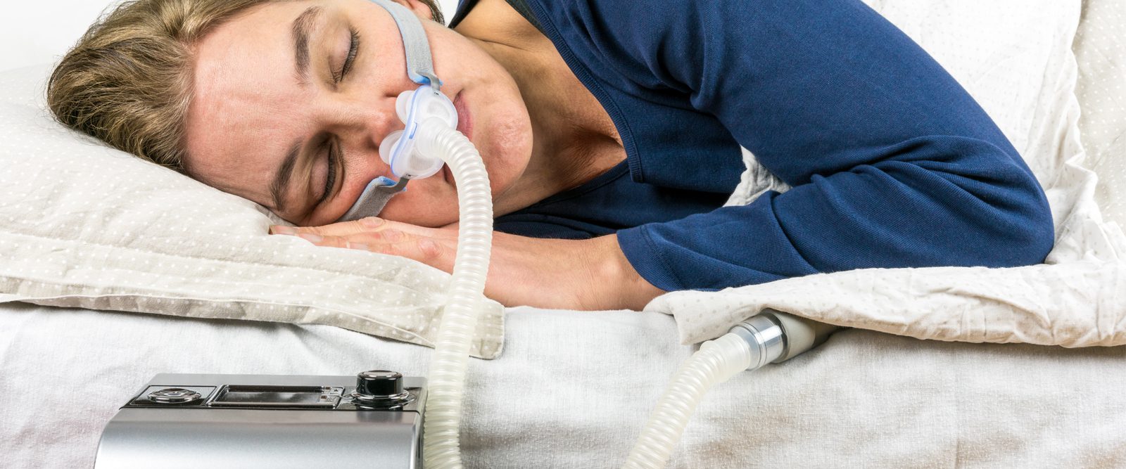 A woman sleeps on her side with a CPAP machine on her face.
