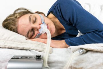 A woman sleeps on her side with a CPAP machine on her face.