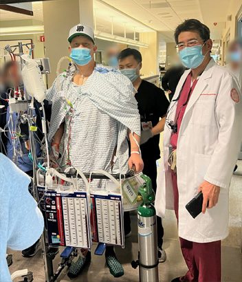 Mati Luik walking in the hospital with medical equipment, accompanied by his doctor and care team.