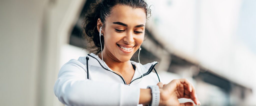 A person wearing earphones looks down at their smartwatch.