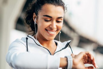 A person wearing earphones looks down at their smartwatch to check their heart rate.