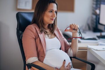 A pregnant person holding a pair of glasses.