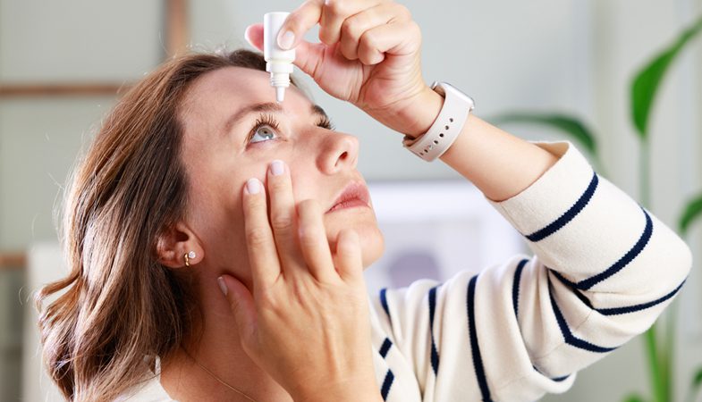 A person putting eye drops into their eye.