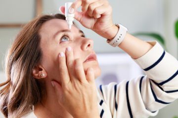 A person putting eye drops into their eye.