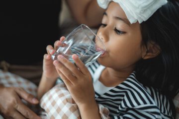 A sick child drinking a glass of water.