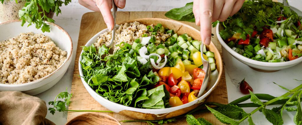 A person making a salad with vegetables and grains.