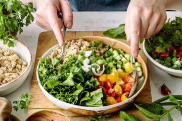 A person making a salad with vegetables and grains.