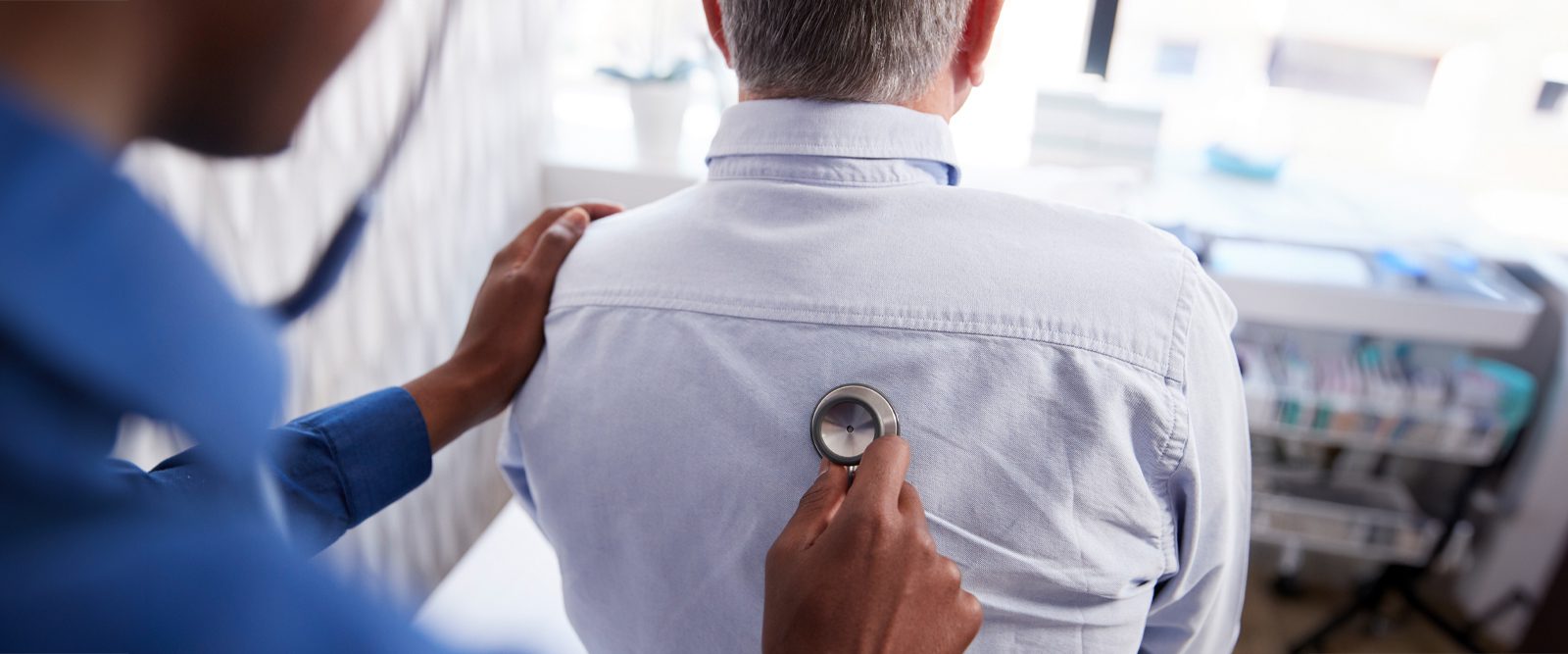 A medical professional holds a stethoscope up to a person's back to listen to their lungs.